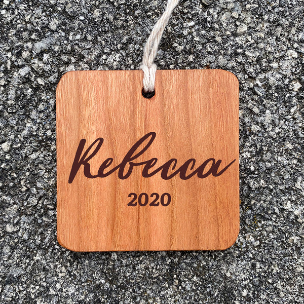Wood ornament with Rebecca 2020 on a concrete background.