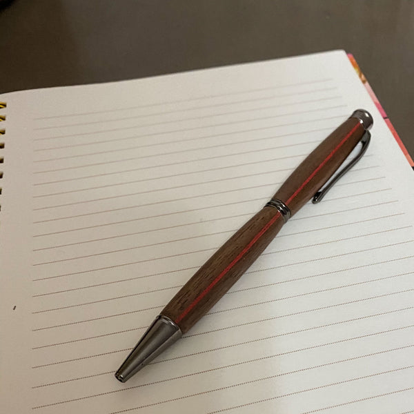 Walnut hand turned pen with a red stripe on a notebook.