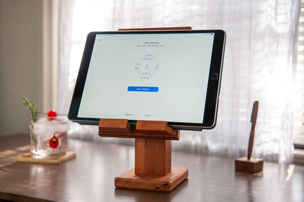 Adjustable wood tablet stand showing with an iPad  at an angle. A cocktail on the left and a wood pen on the right in  a stand.
