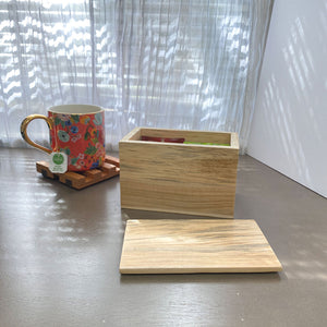 Light maple wood box with the lid next to it, tea bags inside. A flowered mug sits on top of a handcrafted wood trivet by Fallen Tree Woodshop.