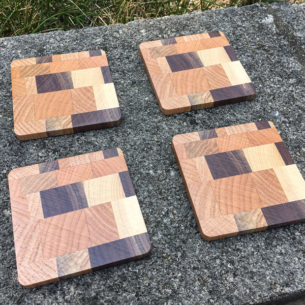 Four wood coaster made from multiple woods sitting on a concrete block