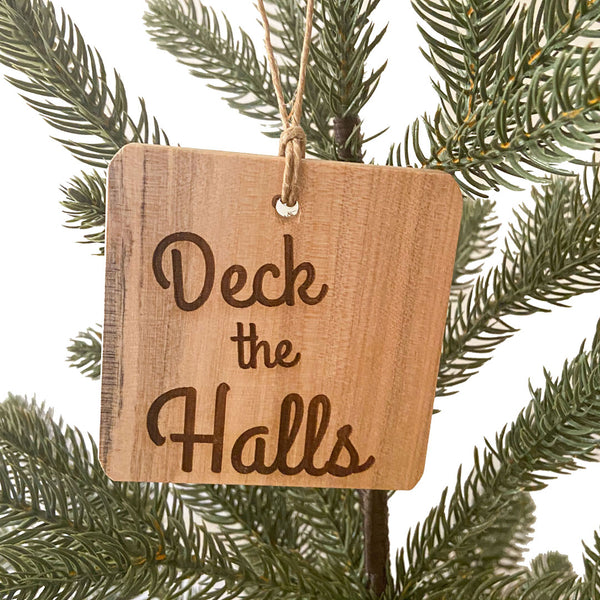 Hand made wood ornament with laser engraved text "Deck the Halls" on a pine tree background. 