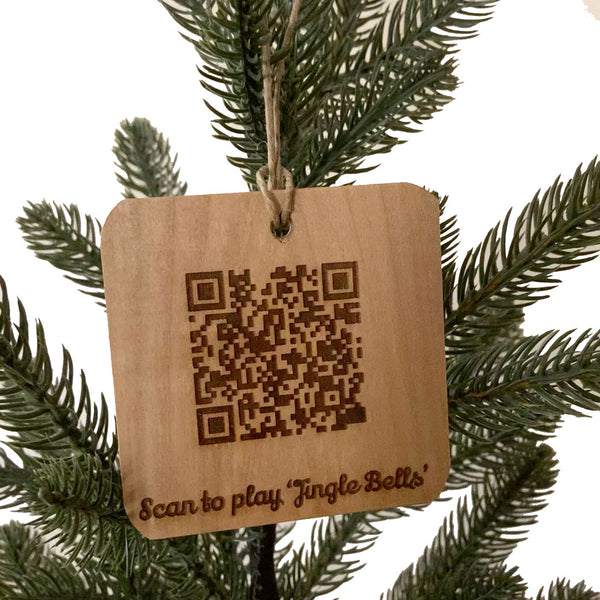 Hand crafted wood ornament from fallen trees with laser engraved QR Code to play Jingle Bells. Hanging on a pine tree with a white background.