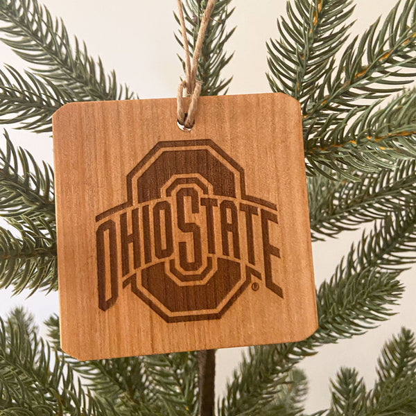 Ohio State Sport Logo laser engraved wood ornament from fallen wood. Set on pine tree background.