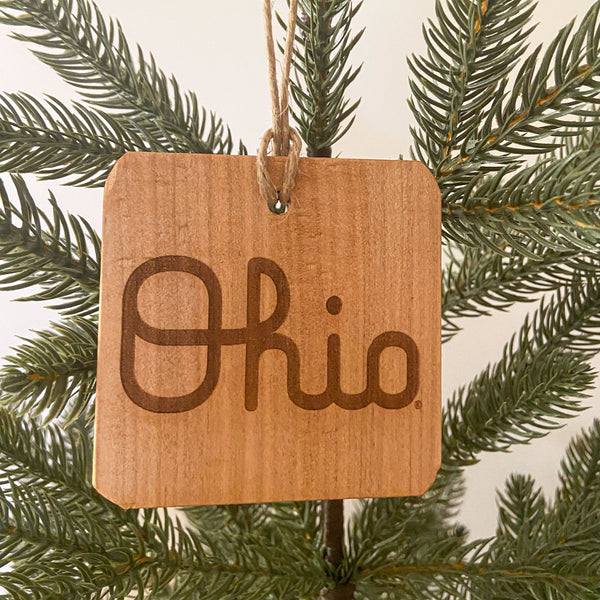 Natural wood ornament with laser engraved OSU Script Ohio. Hanging from a pine tree