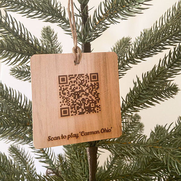 Laser engraved QR Code and text "Scan to play 'Carmen Ohio' OSU natural wood ornament hanging from a pine tree.