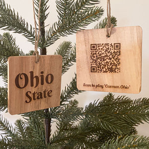 Natural wood ornament with Ohio State Laser engraved. The back of the ornament is shown next to it with a laser engraved QR Code to play the OSU song 'Carmen Ohio'. Hanging from a pine tree.
