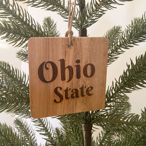 Ohio State natural wood ornament with laser engraved Ohio State text. Hanging from a Pine Tree.