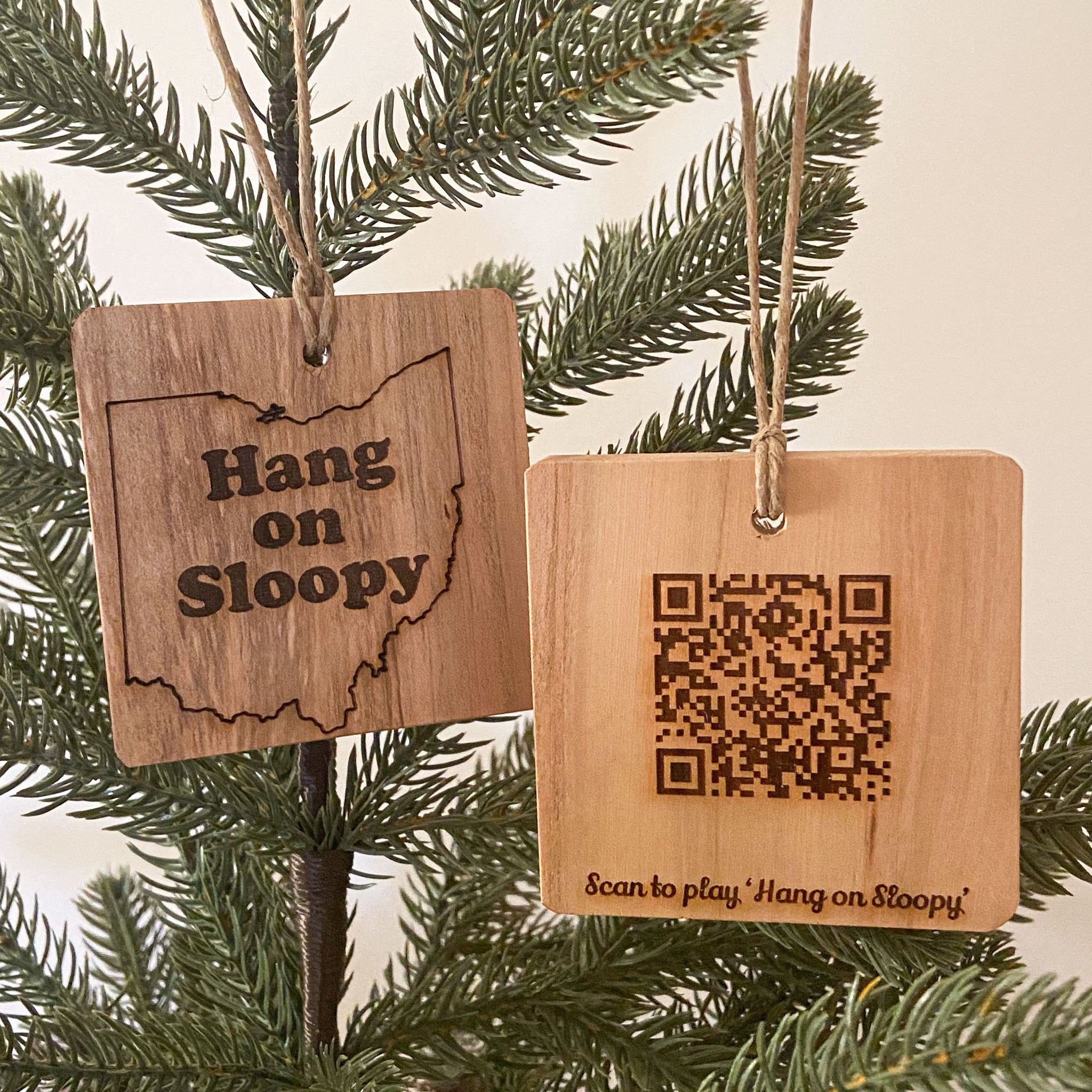 Hang on Sloopy wood ornament shown front and back. Front with Hang on Sloopy text in Ohio state outline, back with QR Code to play the song. Wood natural ornaments on pine tree background.