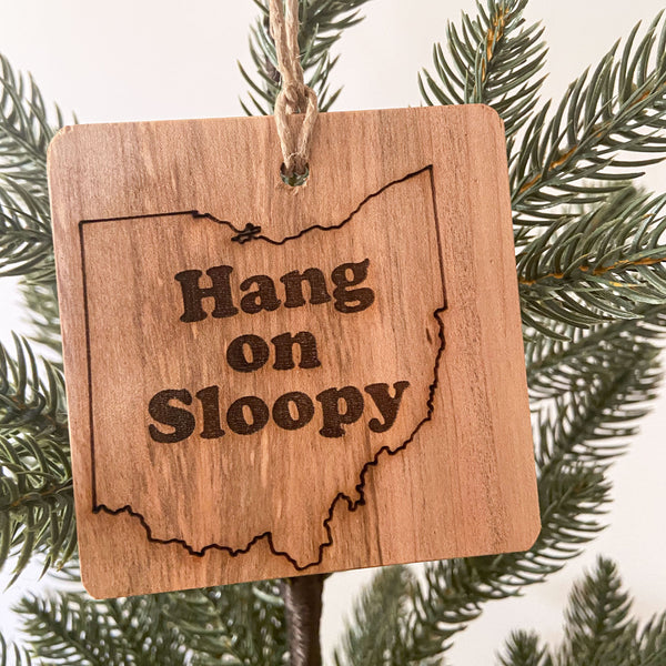 Hand cut natural wood ornament with laser engraved Hang On Sloopy text enclosed in an outline of the state of Ohio. Hanging from a pine tree with a white background.