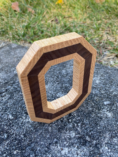 Freestanding handmade wood block O, with dark wood in the center. Set on a concrete background. Shown from above and to the side.