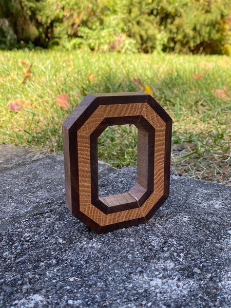 Freestanding handmade wood block O, with light wood in the center. Set on a concrete background.