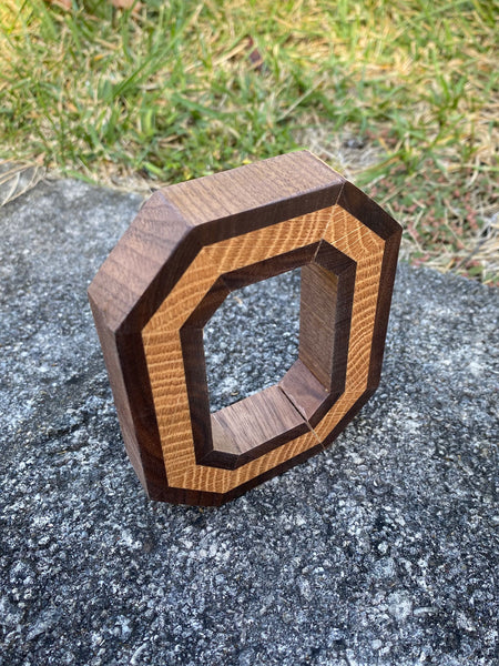 Freestanding handmade wood block O, with light wood in the center. Set on a concrete background. Shown from above.
