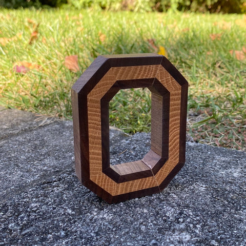 Freestanding handmade wood block O, with light wood in the center. Set on a concrete background.