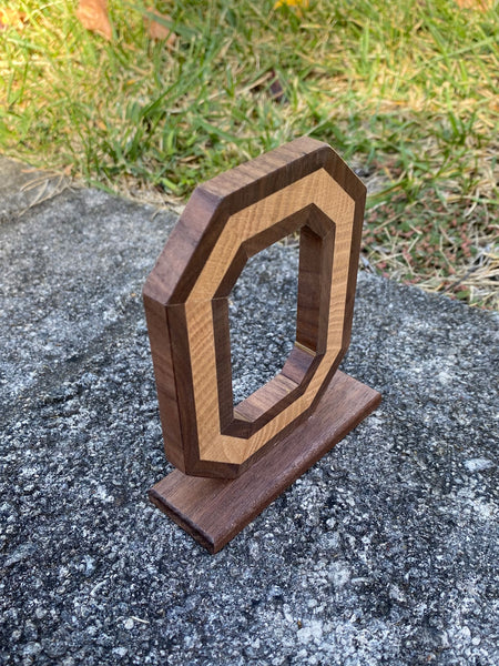 Top angle of a handmade wood block o with a light center and walnut wood dark wrap on a grass background.