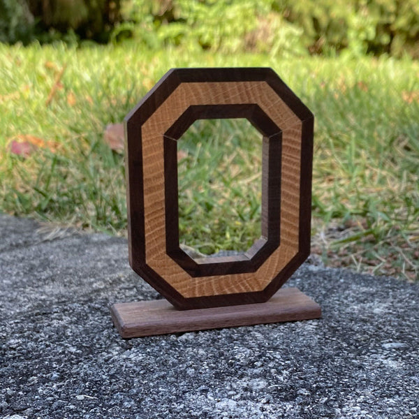 Handmade wood block o with a light center and walnut wood dark wrap on a grass background.
