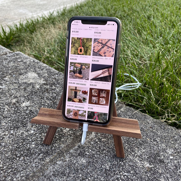 Walnut wood phone stand, easel. Displayed with a phone and charging access.