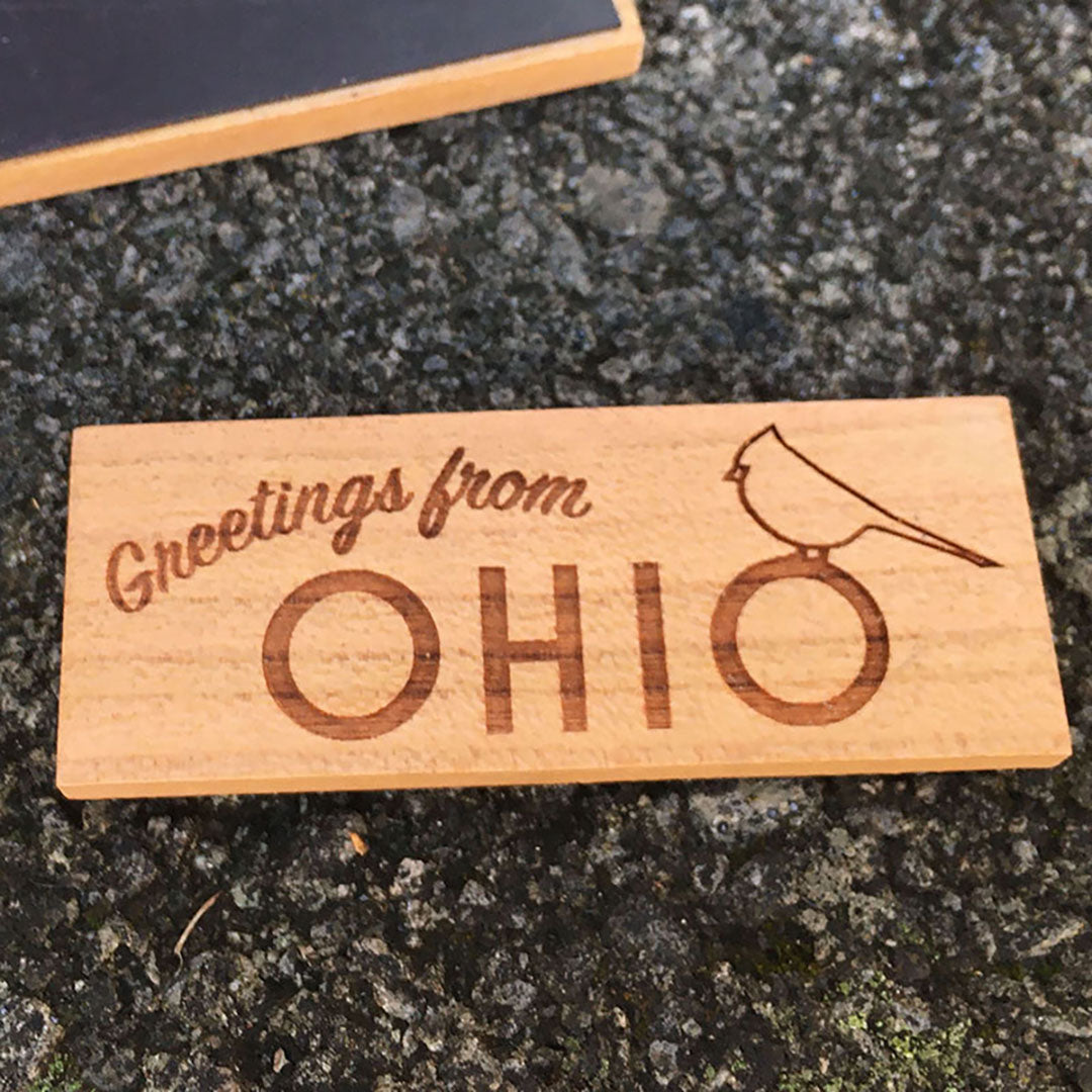 Wood magnet with "Greetings from Ohio" engraved and a cardinal. One concrete background.