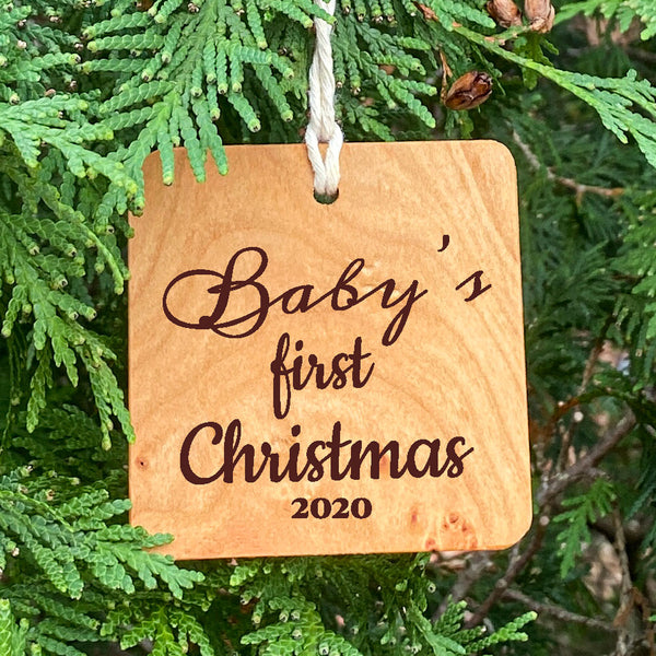 Baby's first Christmas wood ornament on pine tree background.