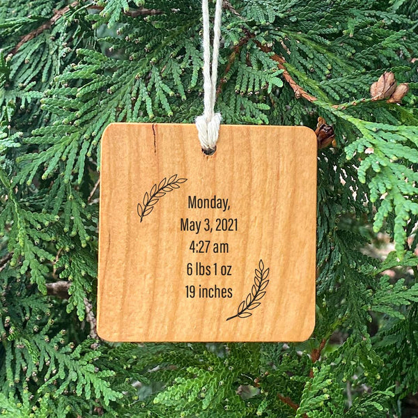 Customized wood ornament with baby stats on wood hanging from a green pine tree.