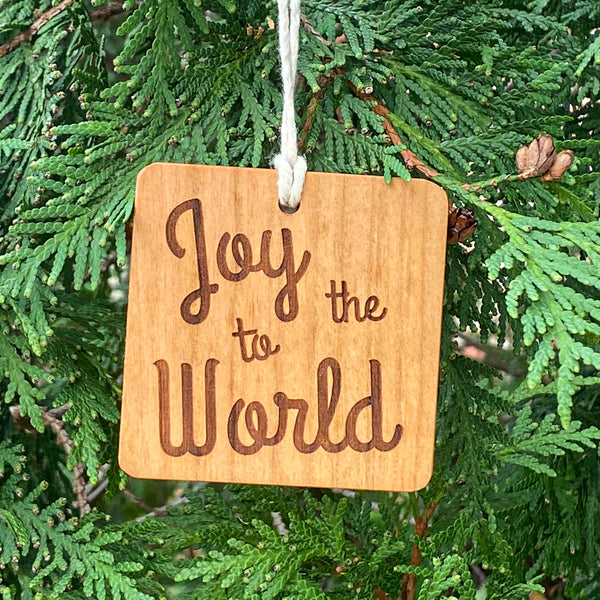 Hand cut wood ornament with Joy to the World laser engraved on a pine tree background.