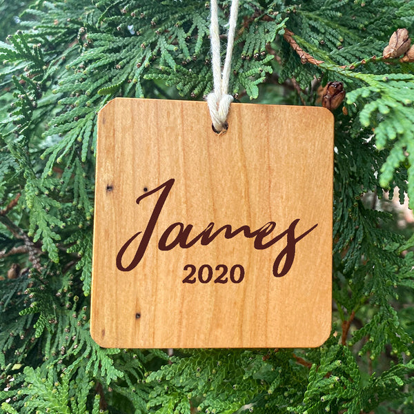 Wood ornament with James 2020 on a pine tree background.