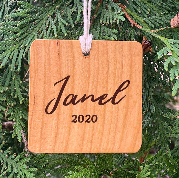 Wood ornament with Janel 2020 on a pine tree background.