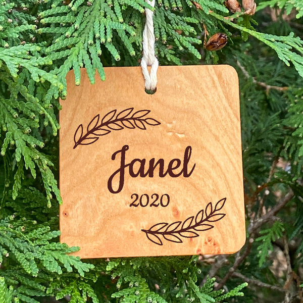 Wood ornament with Janel 2020 and leaves on a pine tree background.
