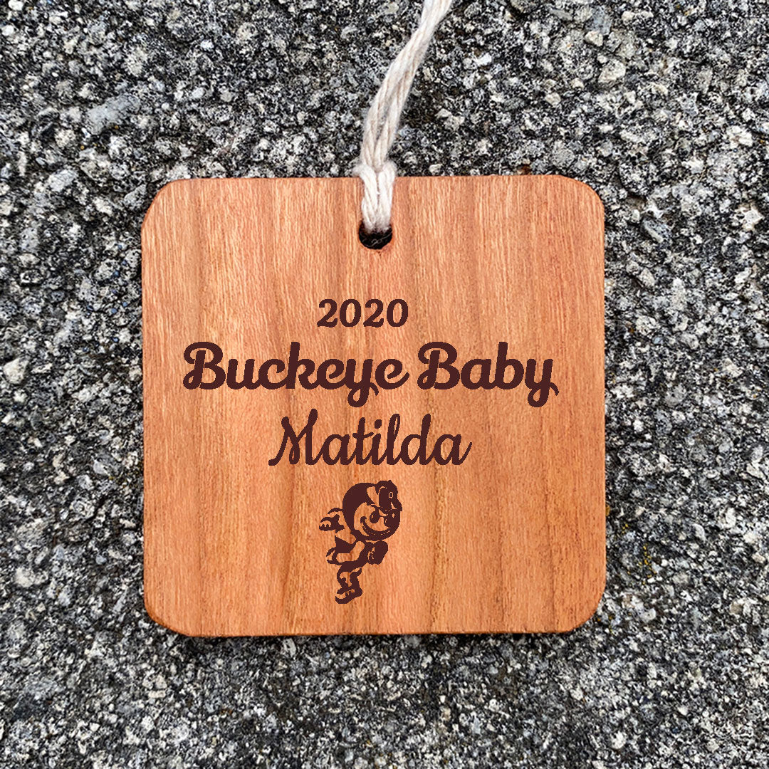Wood Ornament with Buckeye Baby Matilda text engraved on concrete background.