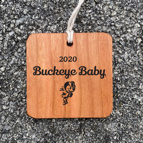 Wood Ornament with Buckeye Baby text engraved on concrete background.