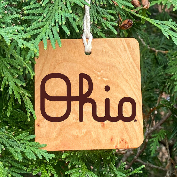 Natural wood ornament with laser engraved OSU Script Ohio. Hanging from a lush pine tree