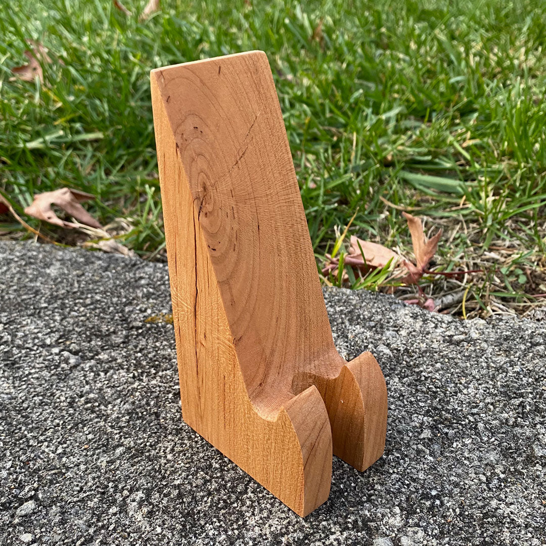 Hand crafted phone stand from fallen cherry, set with a grass background.