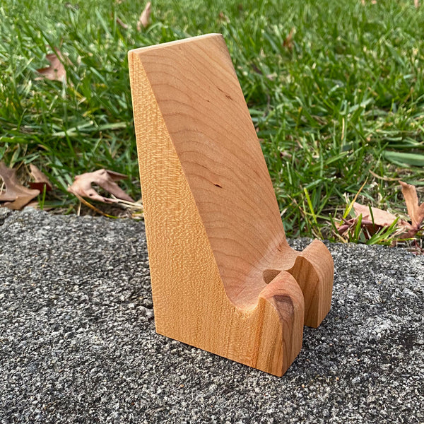 Hand crafted phone stand from fallen cherry, set with a grass background.
