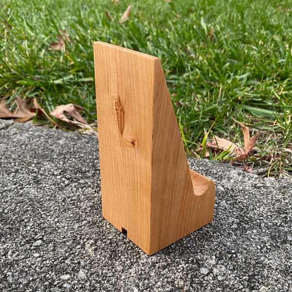 Hand crafted phone stand from fallen cherry, set with a grass background. Shown from back with natural wood.