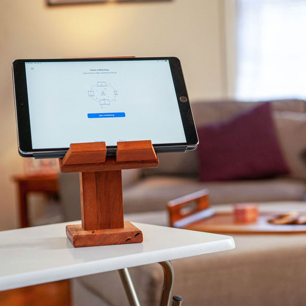 Wood tablet stand with an iPad displaying a Zoom Call. Couch and ottoman in the background
