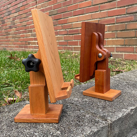 Hand crafted adjustable wood tablet stand made from cherry wood. Two facing each other showing the knob and hinge, set on a brick background.