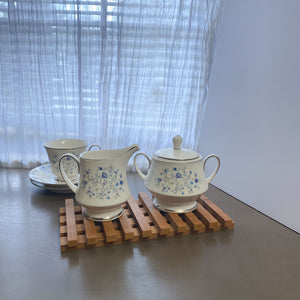 Wood trivet with creamer and sugar porcelain on top.