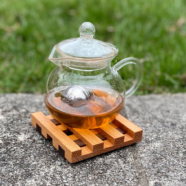 Small square wood trivet, a steaming teapot rests upon it.