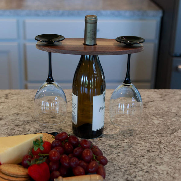 Walnut wood wine display with two wine glasses hanging and a wine bottle in the middle. Fruit and cheese plate in front.
