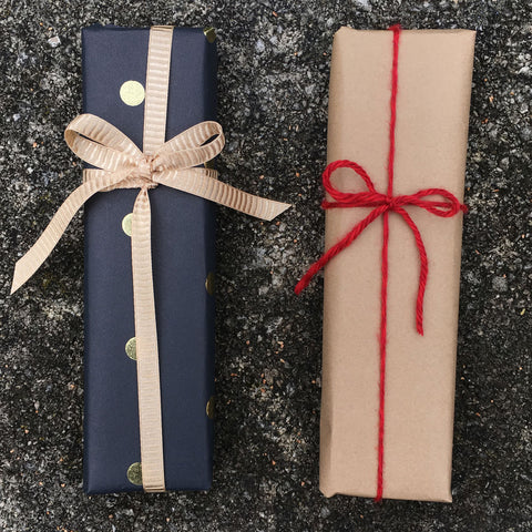 Two small rectangle gifts on a concrete background. Black with gold dots with gold ribbon and craft brown paper with red yarn.