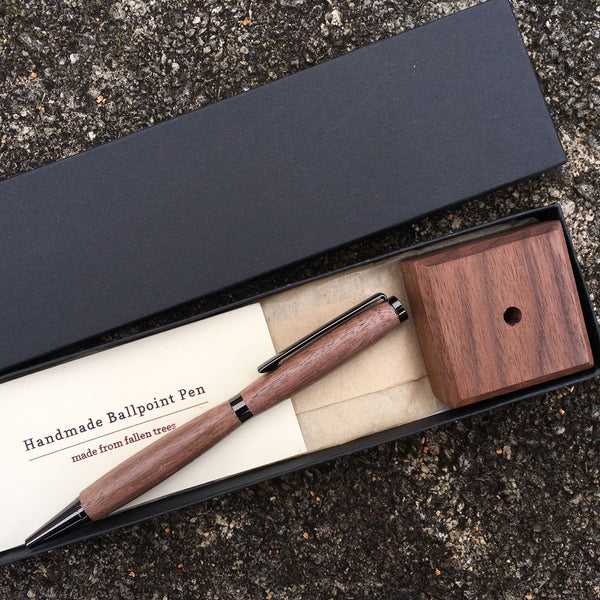 Hand turned walnut pen with coordinating display block. In a black gift box on a concrete background.
