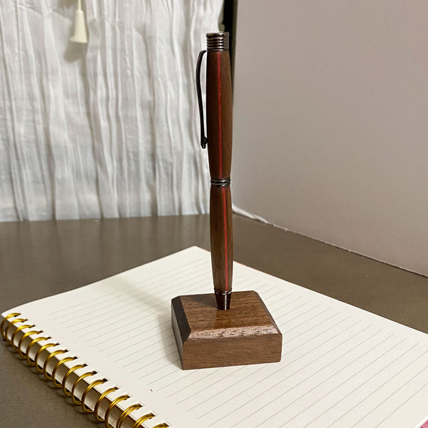Walnut hand turned pen with a red stripe on a stand on a notebook.