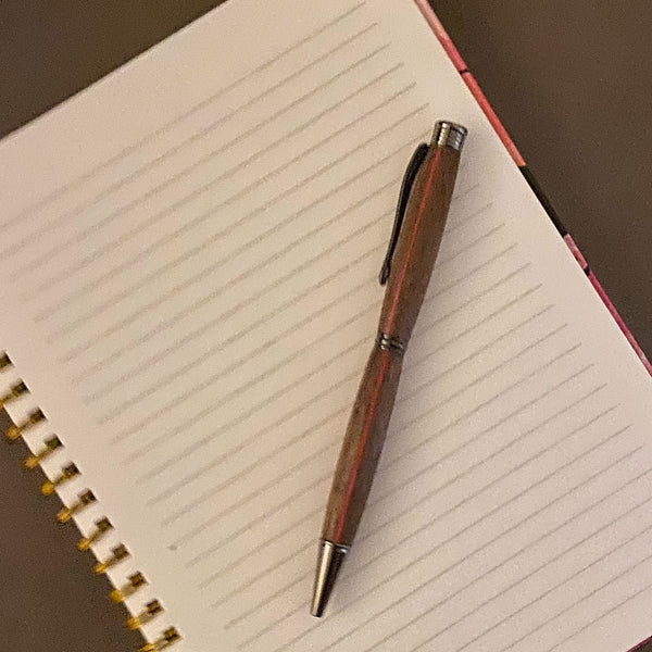 Walnut hand turned pen with a red stripe on a notebook.