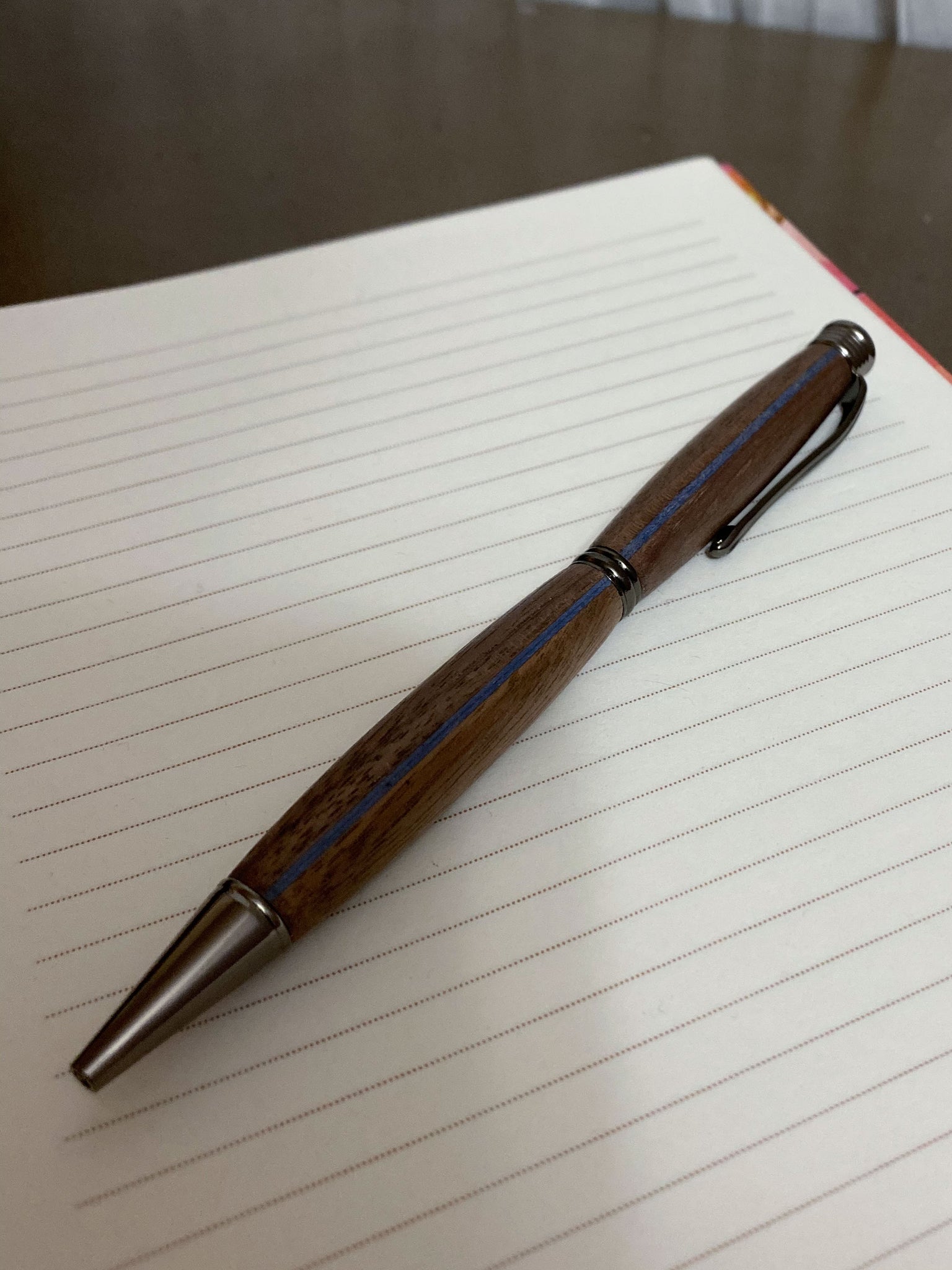 Walnut hand turned pen with a blue stripe on a notebook.