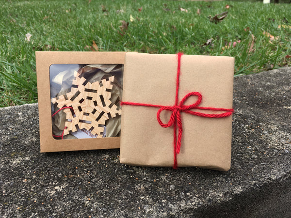 Handmade wood snowflake in a craft window box. Next to the same box wrapped in brown craft paper tied with red yarn in a bow.
