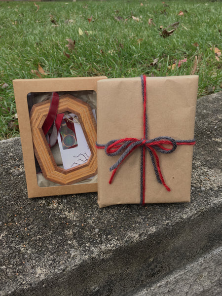 Block O Ornament in a craft window box next to another box (same box) shape in a brown craft paper tied with scarlet and grey yarn and a bow.