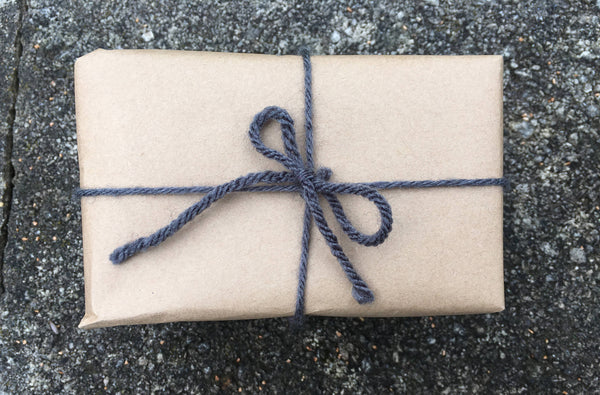 Rectangle gift wrapped in brown craft paper tied with grey yarn bow.