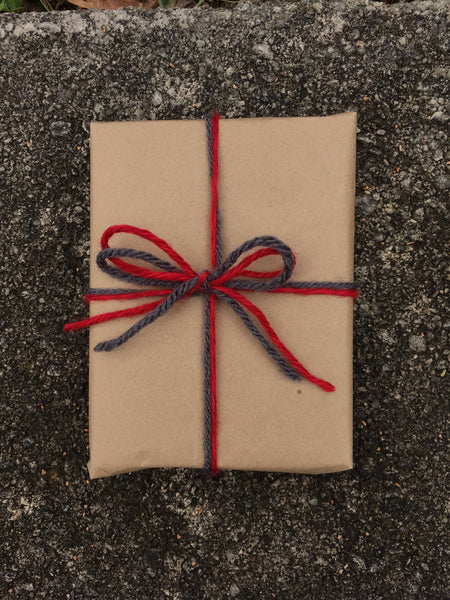 Rectangle gift wrapped in brown craft paper tied with scarlet and grey yarn in a bow.