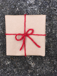 Square wrapped gift in brown craft paper tied with a red yarn bow.