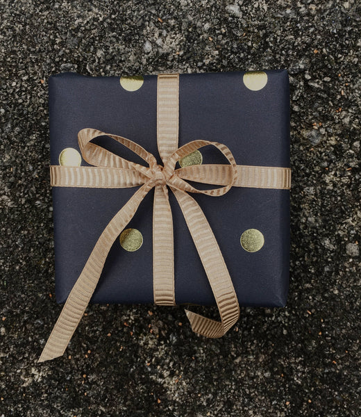 Square small gift wrapped in black paper with gold dots and a gold ribbon.